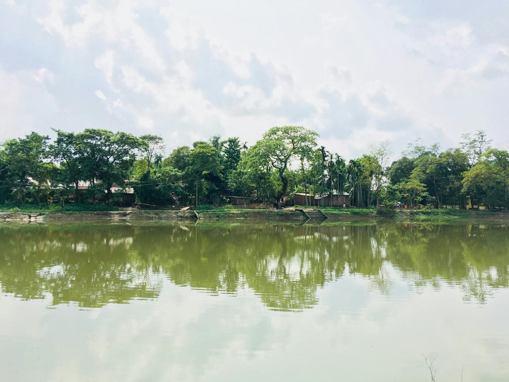 body of water near trees under cloudy sky