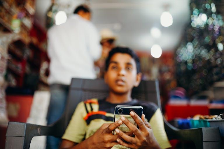 A young boy focused on his smartphone indoors with a blurred background.