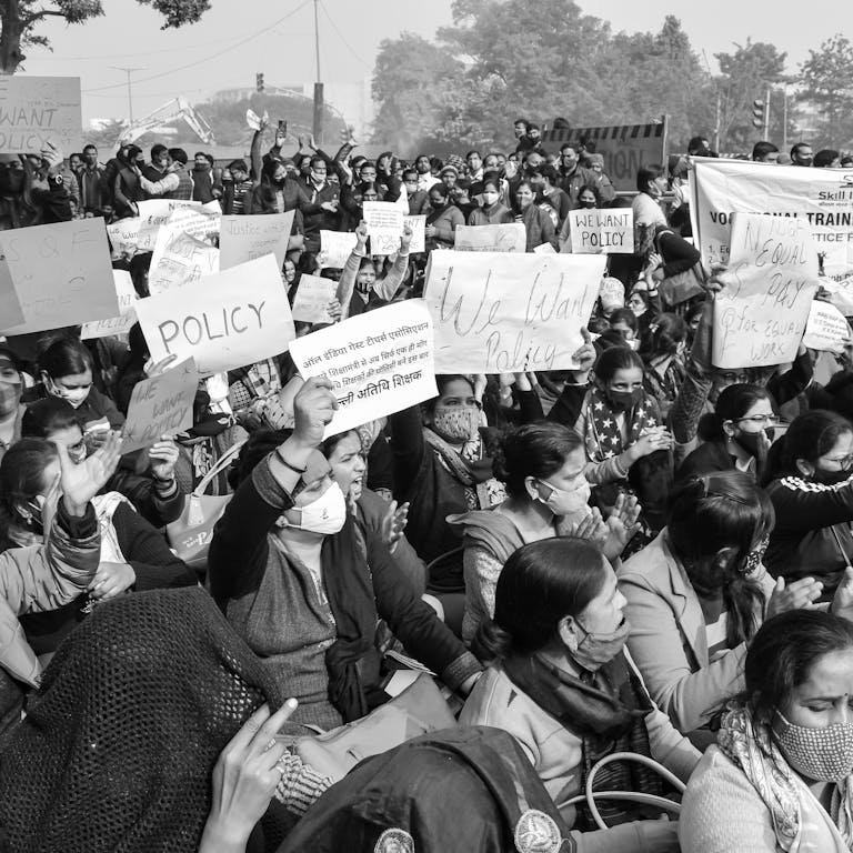 A powerful black and white image of a large protest rally demanding policy change in India.