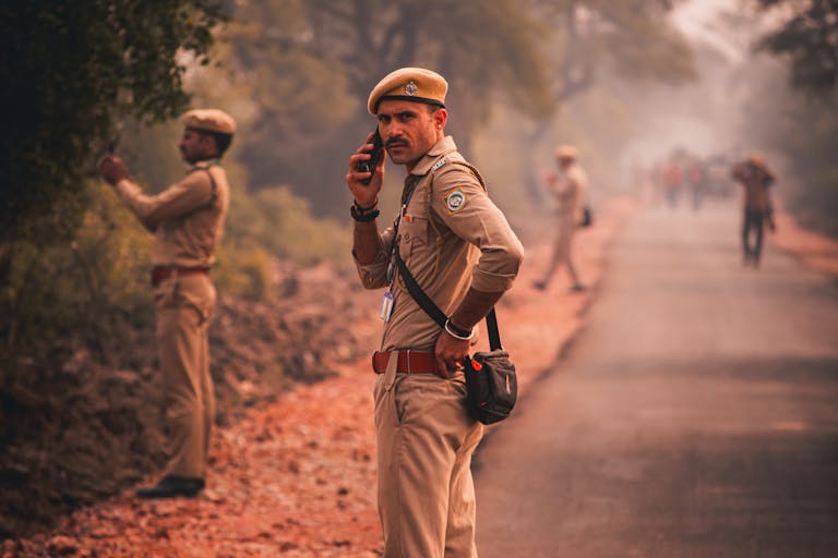 Indian police officer using phone on a rural road with colleagues.