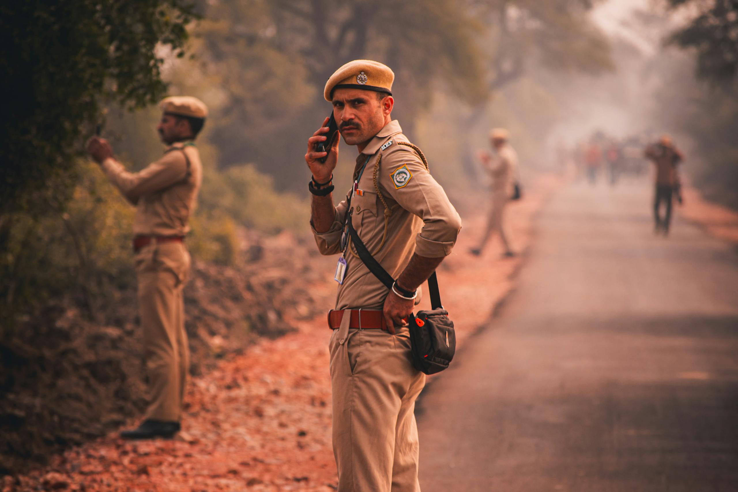 Indian police officer using phone on a rural road with colleagues.